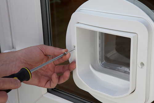 A cat flap being fitted into a glass panel with a screwdriver